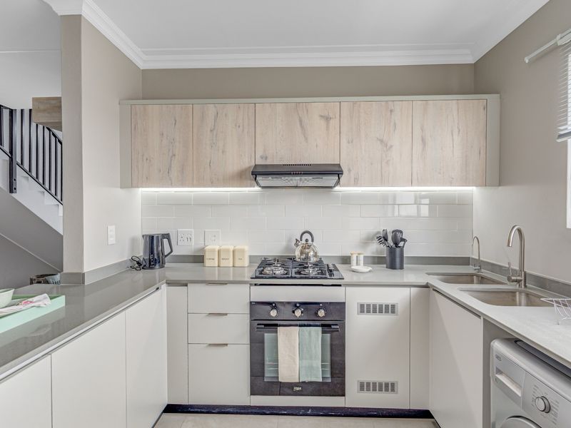 Modern kitchen featuring light wood-grain upper cabinets, white lower cabinetry, stone countertops, gas hob, built-in oven, and a stylish subway tile backsplash.