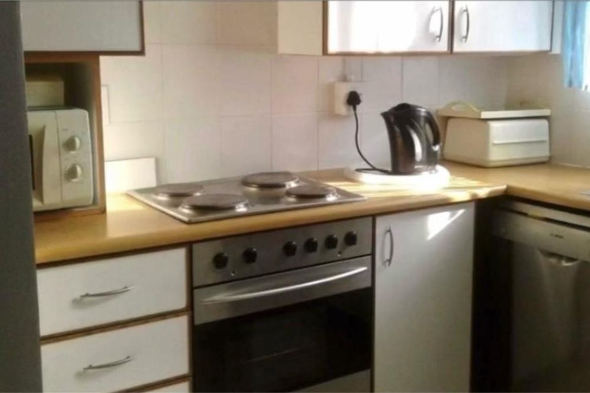 A functional kitchen featuring built-in cabinetry, a laminate countertop, an electric hob, an oven, and a tiled backsplash.