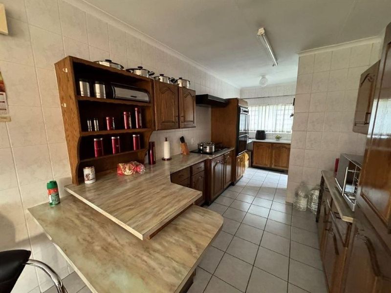 A functional kitchen featuring traditional wooden cabinetry, laminate countertops, ceramic wall and floor tiling, and integrated cooking appliances.