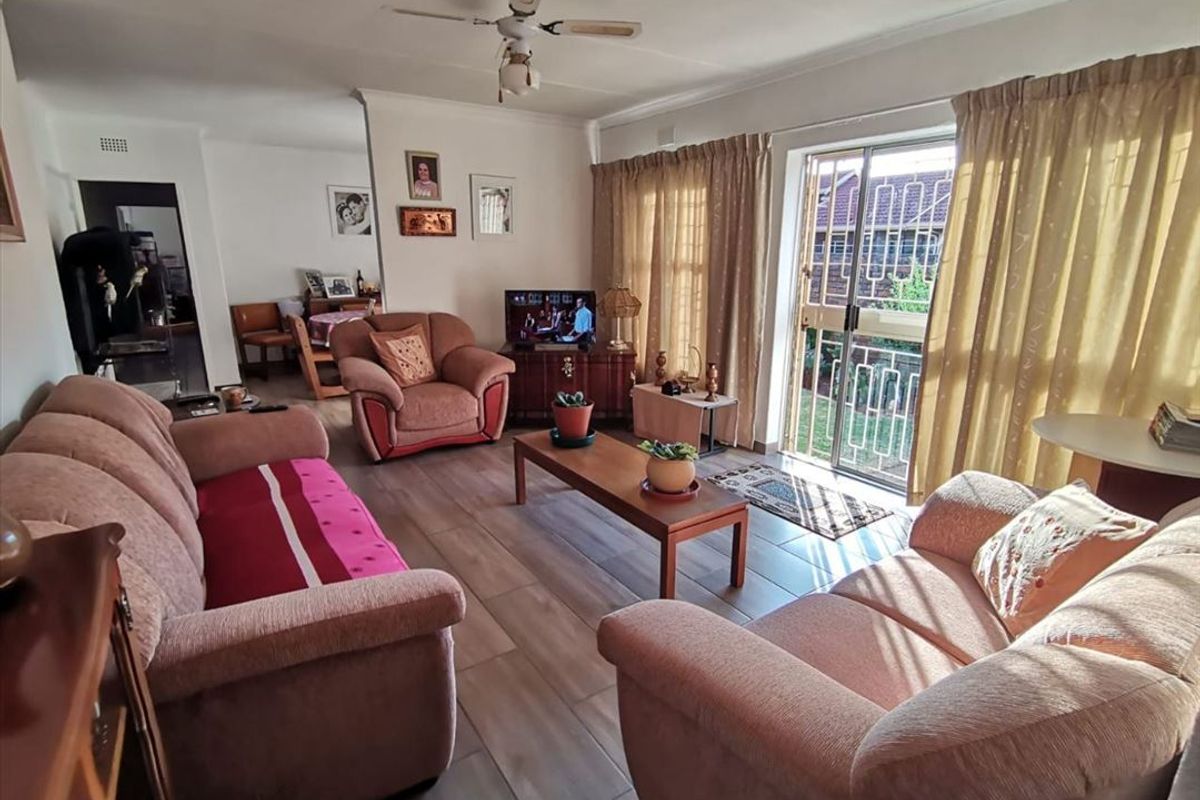 A comfortable living room featuring tiled flooring, a ceiling fan, and a sliding glass door with a security gate leading to the exterior.