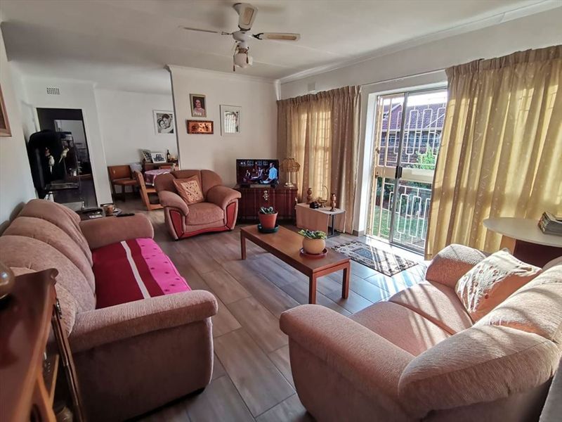 A comfortable living room featuring tiled flooring, a ceiling fan, and a sliding glass door with a security gate leading to the exterior.