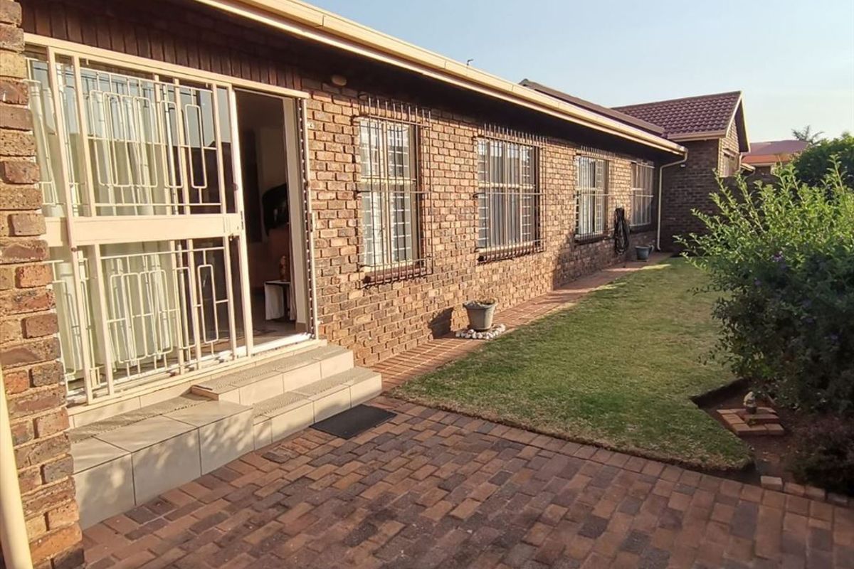 Rear exterior view of the townhouse featuring a face brick facade, paved patio area, and a well-maintained lawn with security features on windows and doors.