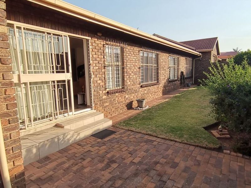 Rear exterior view of the townhouse featuring a face brick facade, paved patio area, and a well-maintained lawn with security features on windows and doors.