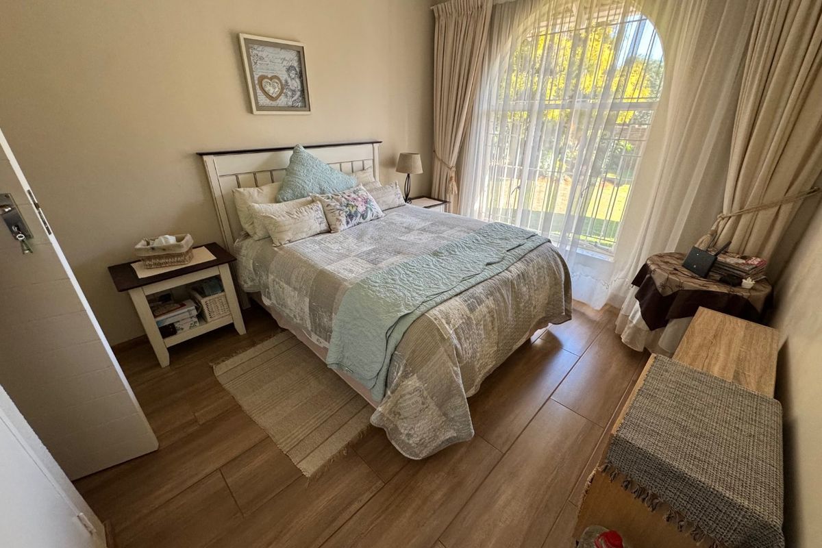 A cozy bedroom featuring wood-look flooring, a large arched window with natural light, and neutral wall finishes.