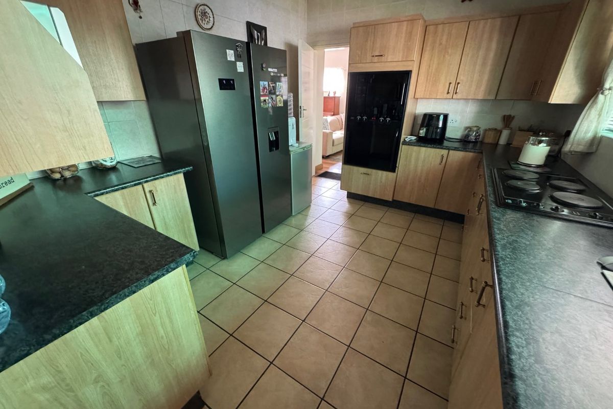 A functional kitchen featuring light wood-finish cabinetry, dark laminate countertops, tiled flooring, and integrated oven and hob appliances.