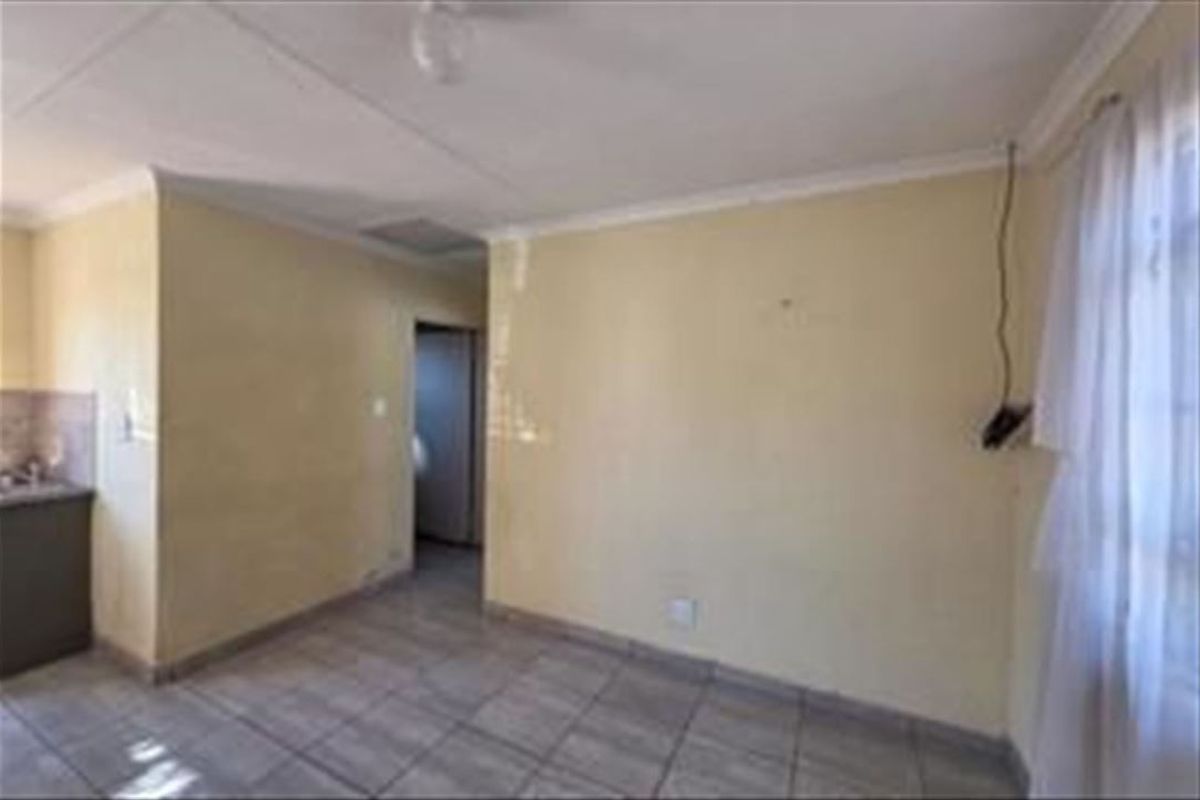 An empty open-plan living area featuring tiled flooring and cornicing, requiring cosmetic updates to the wall finishes and electrical fixtures.
