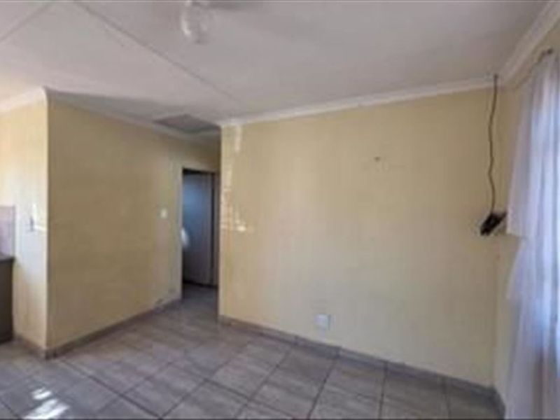An empty open-plan living area featuring tiled flooring and cornicing, requiring cosmetic updates to the wall finishes and electrical fixtures.