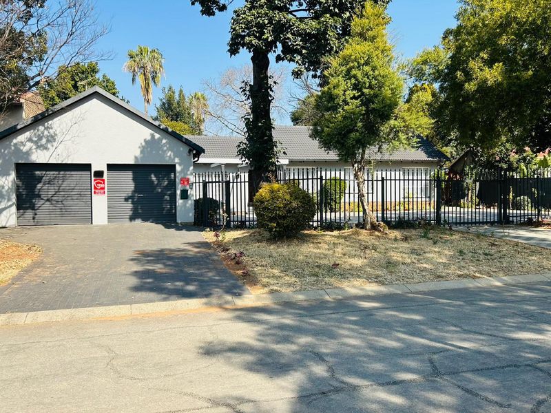 Front view of the property featuring a double garage, paved driveway, and secure metal fencing surrounding the front garden area.