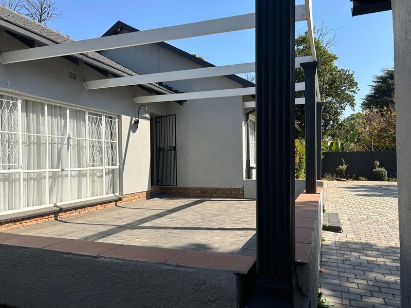 A paved outdoor patio area featuring a pergola structure, security gate, and brick wall detailing, providing a functional space for outdoor living.