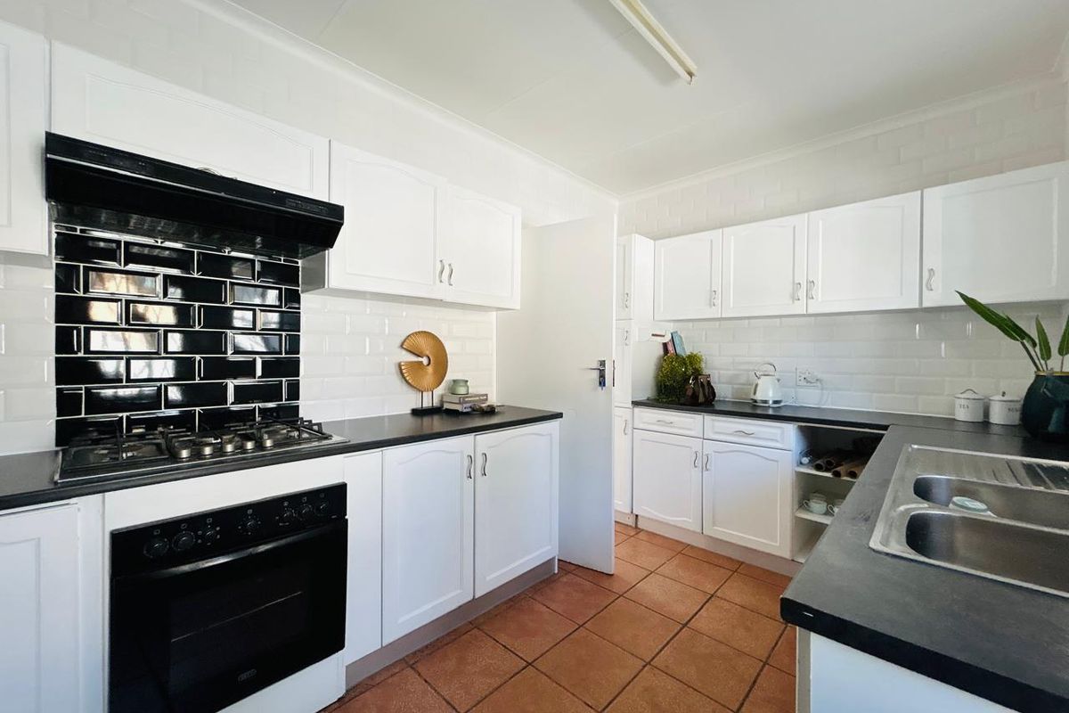 A functional kitchen featuring white cabinetry, contrasting black subway tile backsplash, gas hob, built-in oven, and durable terracotta floor tiles.