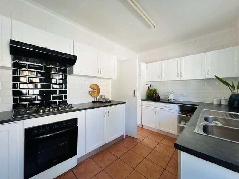 A functional kitchen featuring white cabinetry, contrasting black subway tile backsplash, gas hob, built-in oven, and durable terracotta floor tiles.
