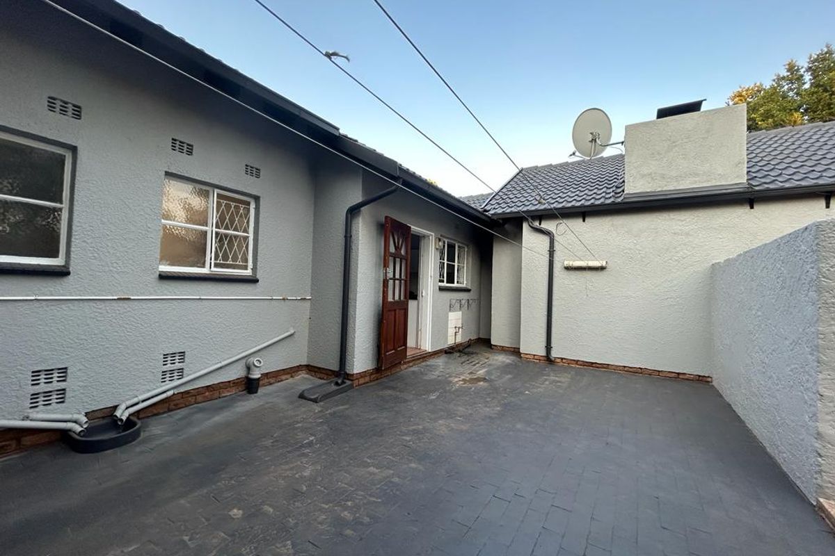A rear courtyard area featuring paved flooring, external drainage infrastructure, and access to the main dwelling via a wooden door.
