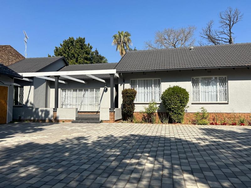 Front elevation of a well-maintained house featuring a paved driveway, a covered pergola entrance, and a tiled roof.