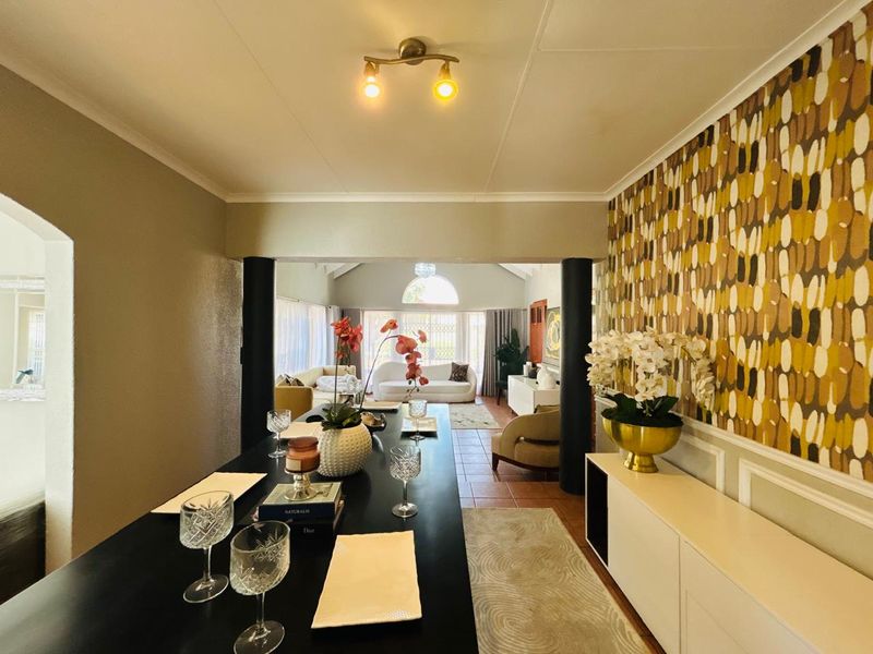 Open plan living and dining area featuring decorative wallpaper, wainscoting, tiled flooring, and an archway leading to a bright lounge space.