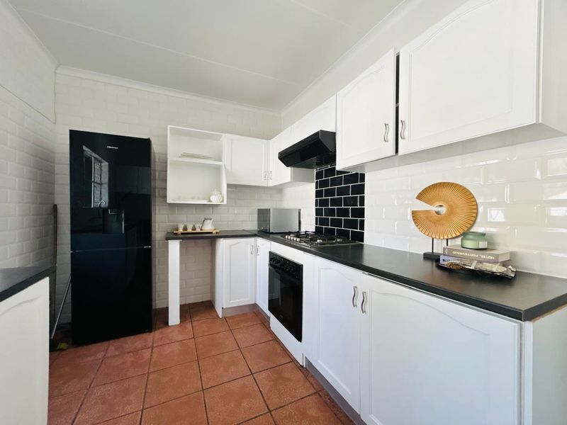 A well-maintained kitchen featuring white cabinetry, black subway tile backsplash, dark countertops, and durable ceramic floor tiles.
