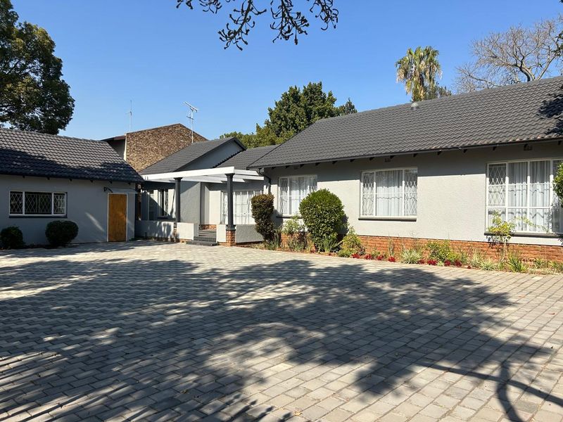 A well-maintained single-story home featuring a paved driveway, tiled roof, and secure entrance area with established garden beds.