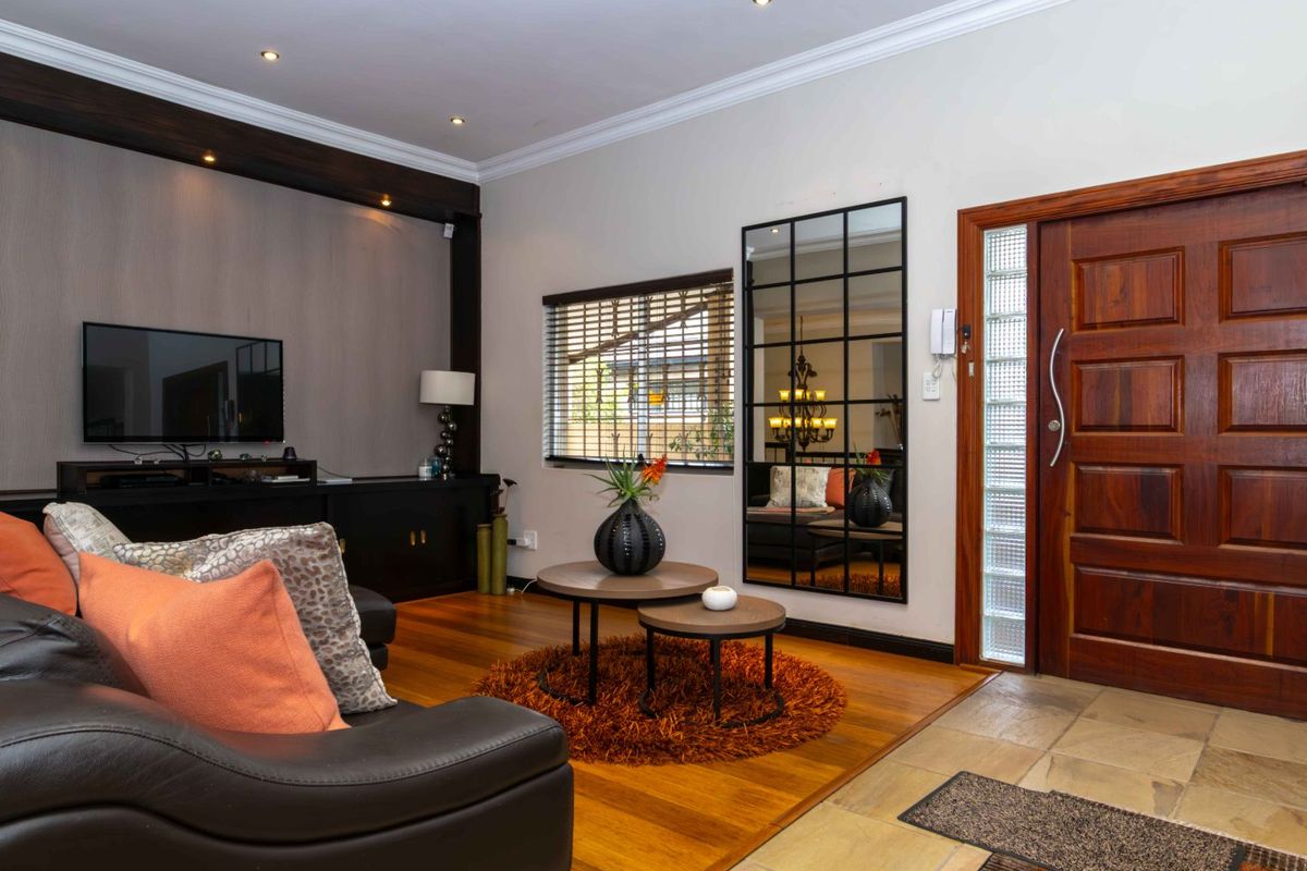 A well-maintained living room featuring timber flooring, recessed lighting, and a solid timber front door with a decorative glass block sidelight.