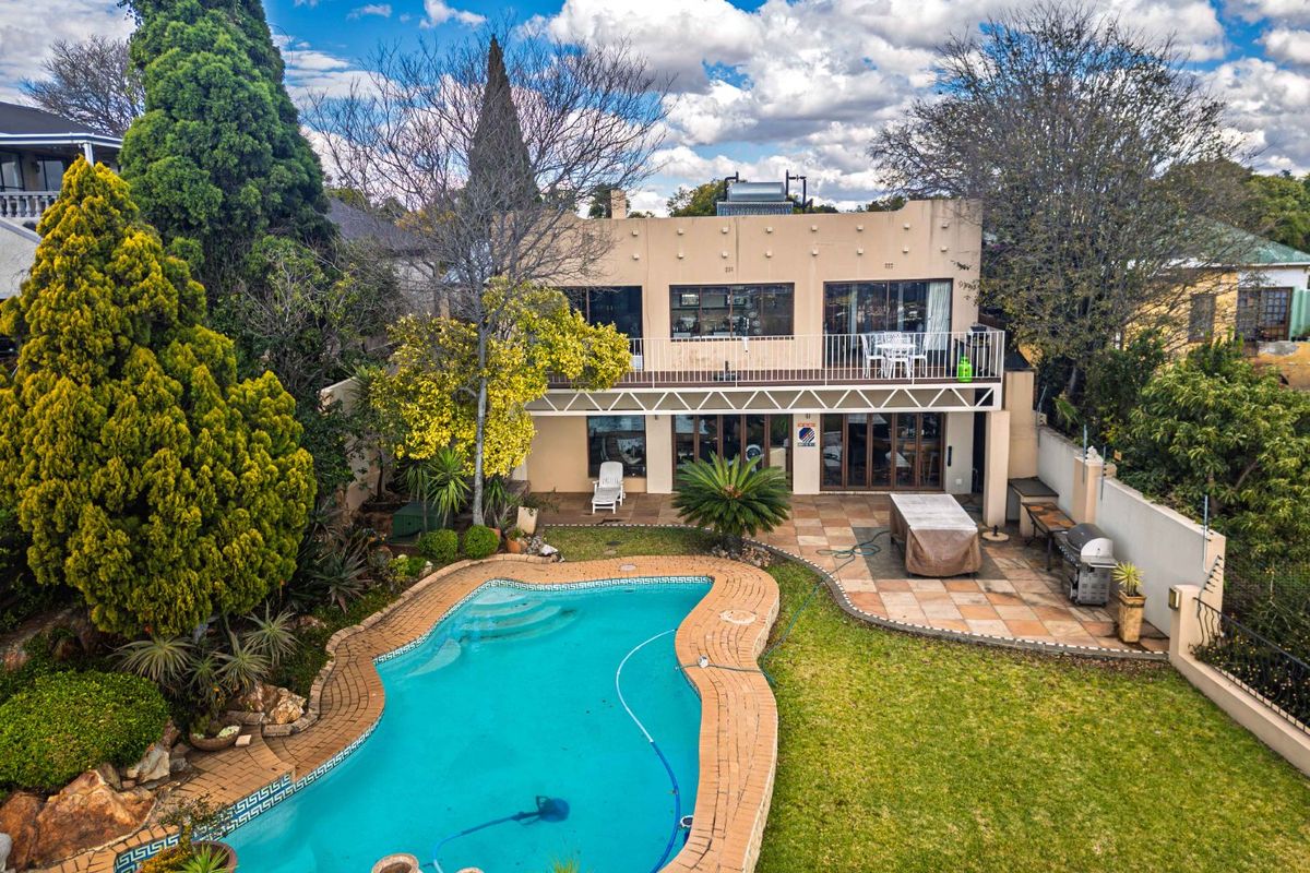 Rear view of the property featuring a swimming pool, paved patio area, and a balcony overlooking the garden.