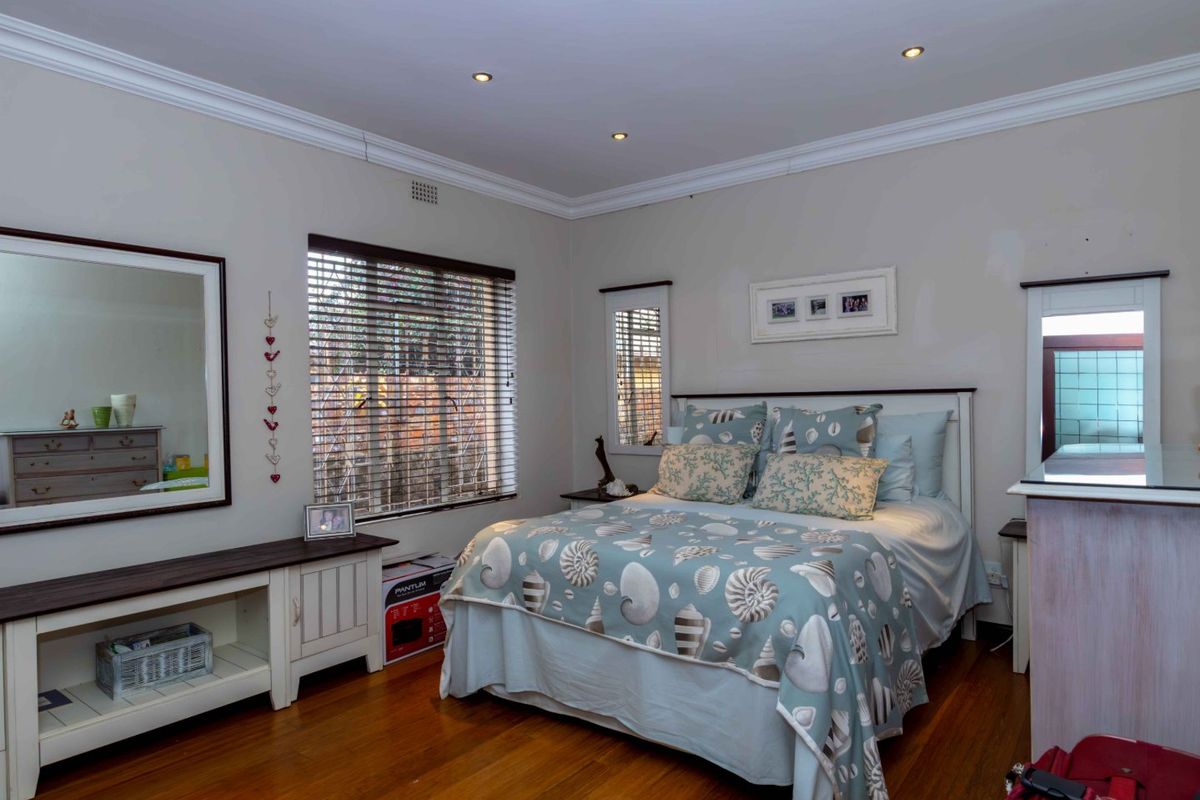 A well-maintained bedroom featuring polished hardwood flooring, recessed ceiling lighting, crown molding, and venetian blinds.