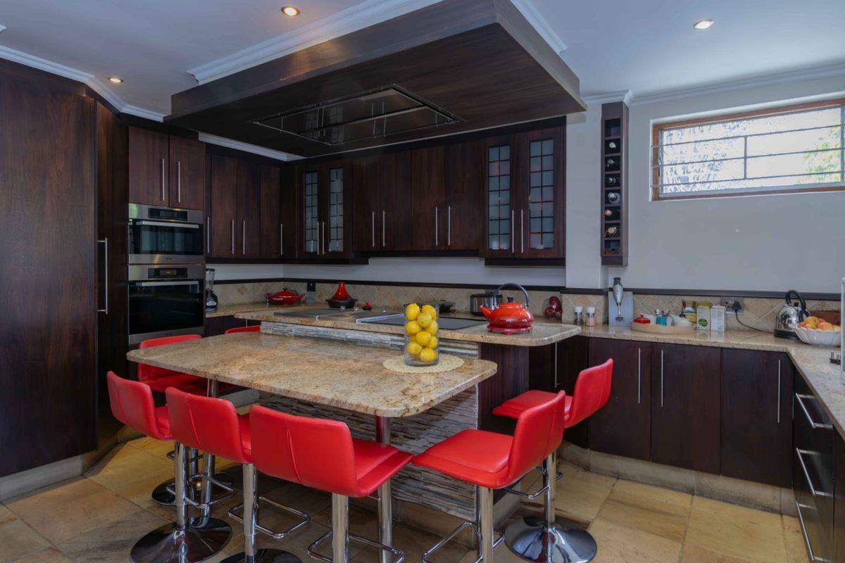 A well-appointed kitchen featuring dark wood cabinetry, granite countertops, a central breakfast bar, and integrated appliances with stone tile flooring.