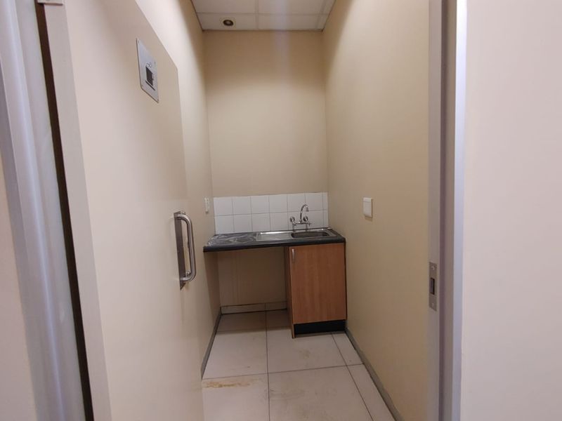 A compact utility scullery area featuring a built-in sink, laminate countertop, tiled splashback, and base cabinetry, suitable for office or commercial use.