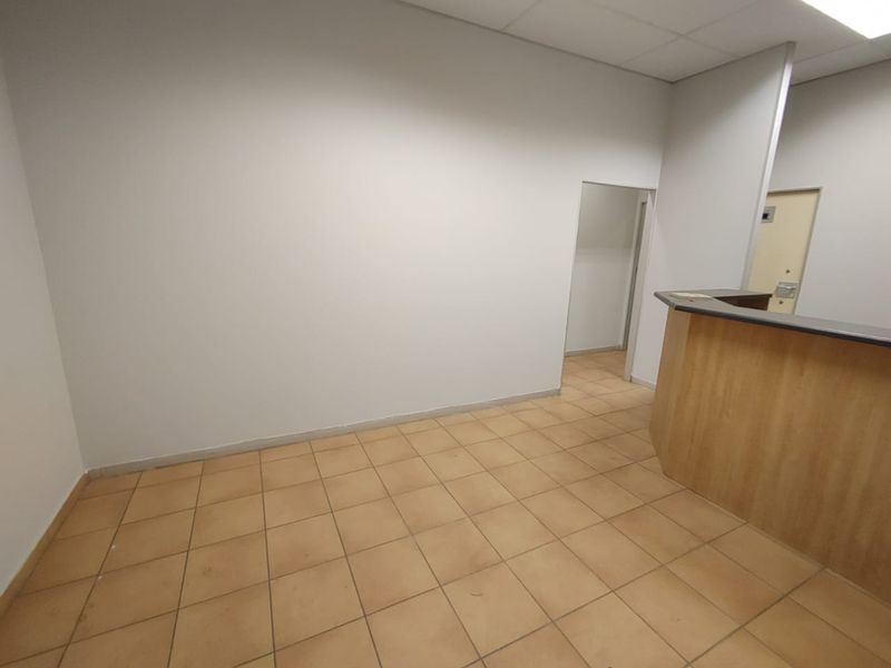 An empty commercial office space featuring tiled flooring, a built-in reception counter, and a suspended ceiling, suitable for various business configurations.