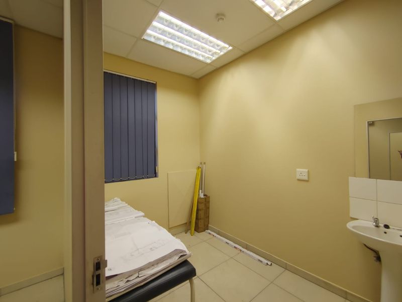 A functional office space featuring tiled flooring, a pedestal sink, recessed lighting, and vertical blinds, offering a clean and practical work environment.