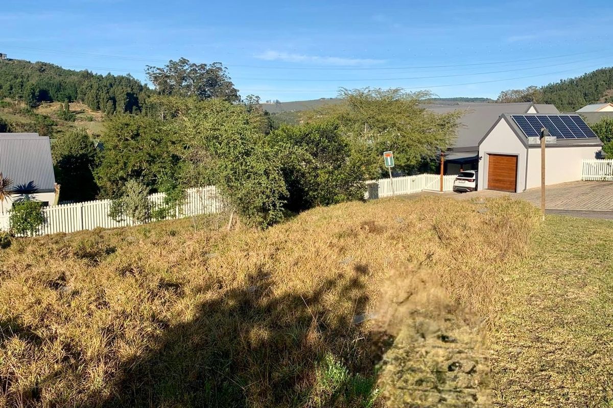 A view of a vacant residential plot with natural grass cover, adjacent to an existing property with a garage and solar panels.