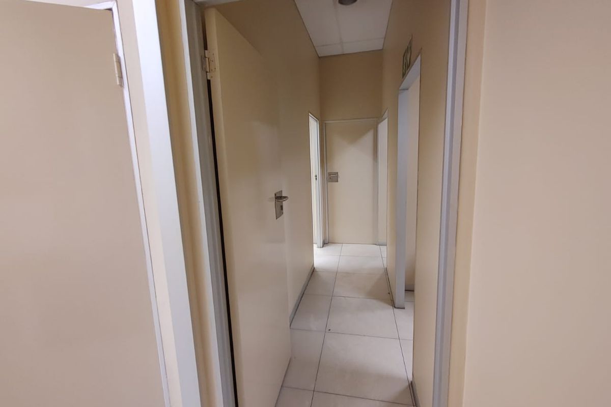 A functional commercial hallway featuring tiled flooring, neutral walls, and multiple internal access doors.