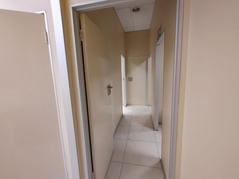 A functional commercial hallway featuring tiled flooring, neutral walls, and multiple internal access doors.