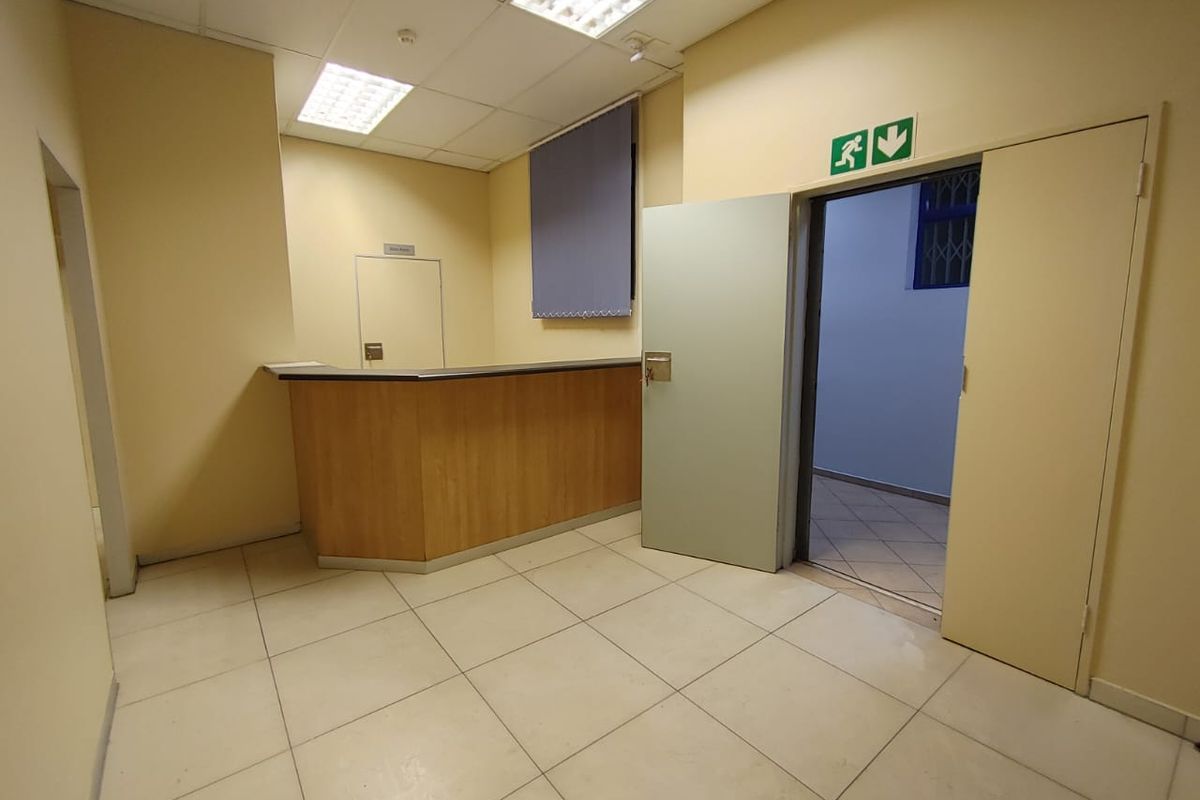 A functional commercial reception area featuring a built-in counter, tiled flooring, and suspended ceiling lighting, suitable for a professional office or service space.