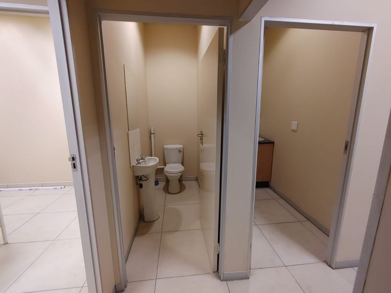 A functional commercial bathroom facility featuring a pedestal sink, toilet, and neutral tiled flooring, presented in a clean and vacant state.