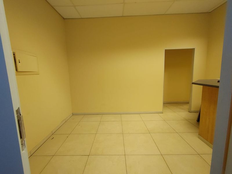 An empty commercial office space featuring tiled flooring, a suspended ceiling, and a built-in service counter, suitable for various business configurations.