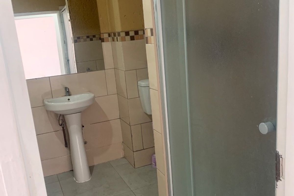 A functional bathroom featuring a pedestal basin, shower enclosure, and tiled finishes, currently in need of cosmetic updates and maintenance.