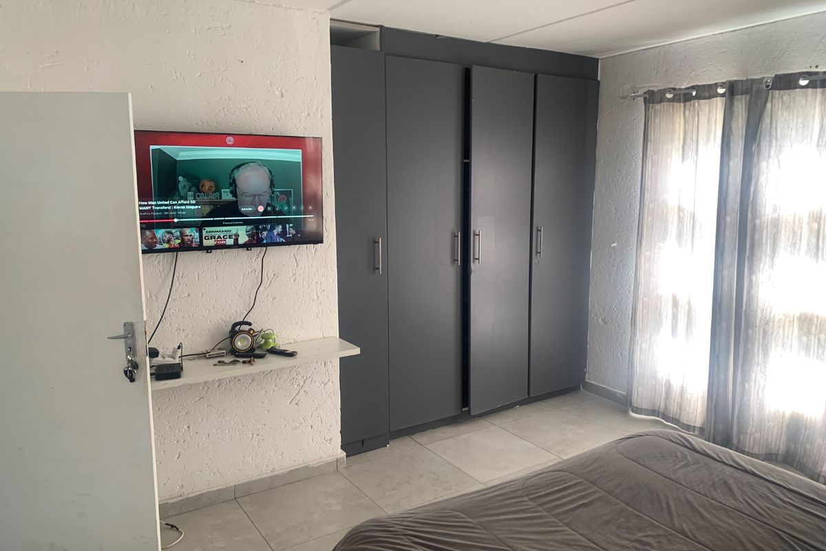 A bedroom featuring tiled flooring, a textured wall finish, and a large dark grey built-in wardrobe.
