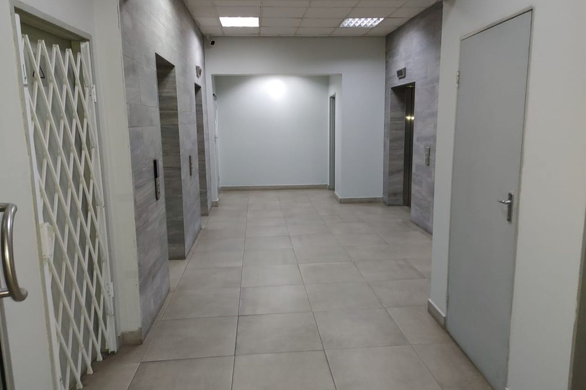 A clean, commercial hallway featuring tiled flooring, recessed lighting, and access to multiple elevators.