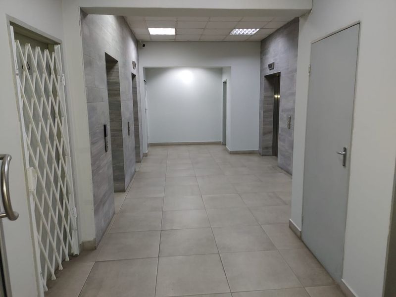 A clean, commercial hallway featuring tiled flooring, recessed lighting, and access to multiple elevators.