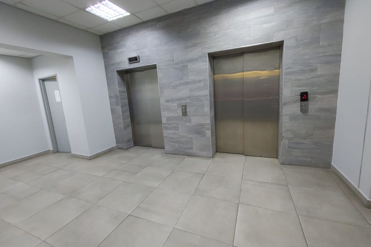 A clean commercial elevator lobby featuring modern stainless steel lift doors, neutral tiled flooring, and contemporary stone-look wall finishes.