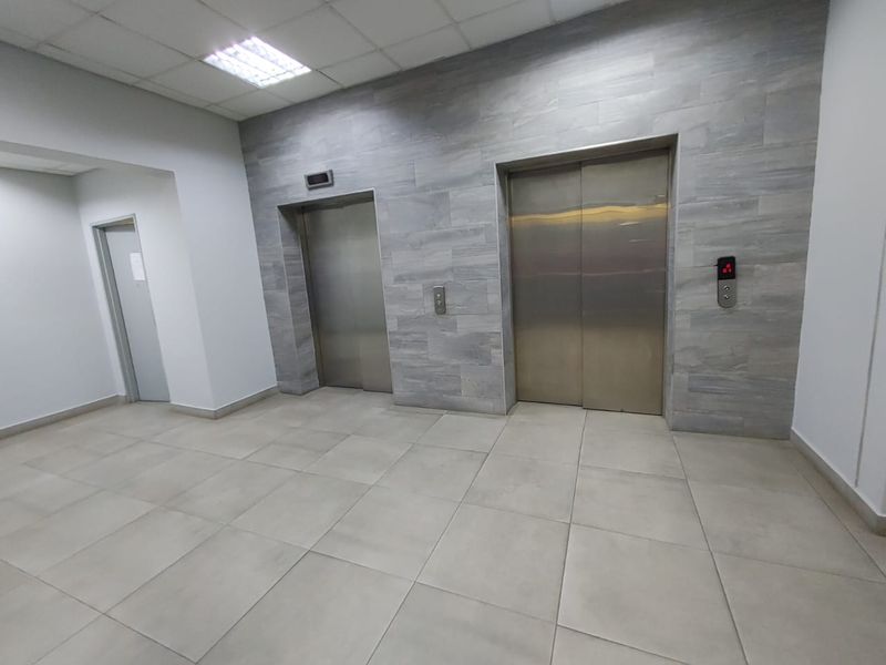 A clean commercial elevator lobby featuring modern stainless steel lift doors, neutral tiled flooring, and contemporary stone-look wall finishes.