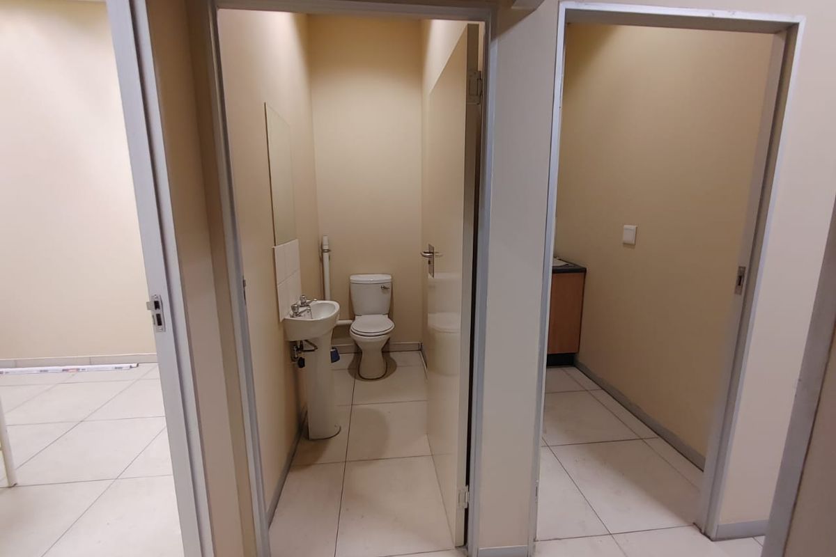 A functional commercial bathroom facility featuring a pedestal sink, toilet, and neutral tiled flooring, presented in a clean and vacant state.