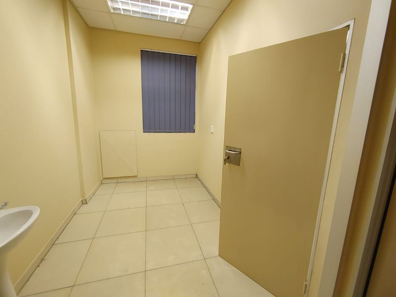 A vacant commercial office space featuring tiled flooring, a pedestal sink, and a drop ceiling with integrated lighting.