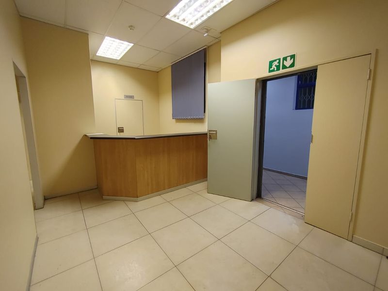 A functional commercial reception area featuring a built-in counter, tiled flooring, and suspended ceiling lighting, suitable for a professional office or service space.