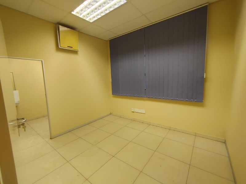 An empty office space featuring tiled flooring, a suspended ceiling with recessed lighting, and vertical window blinds.