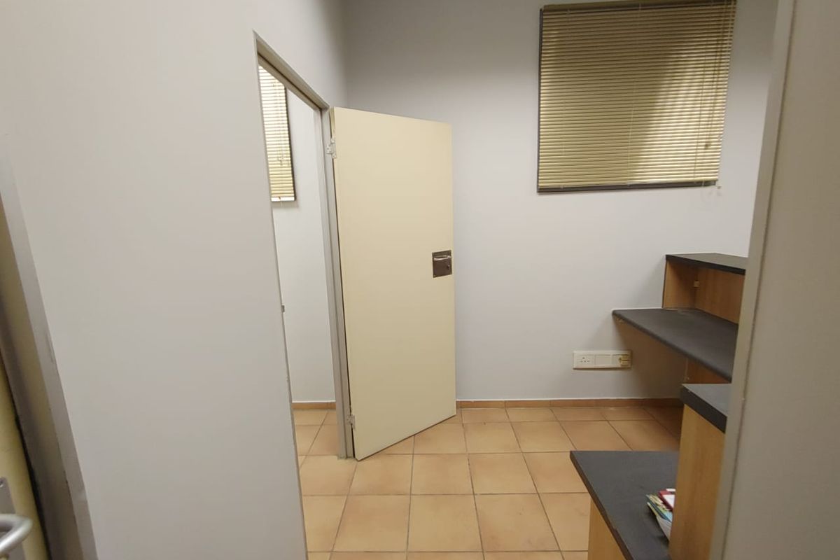 A functional office space featuring built-in desk cabinetry, tiled flooring, and window blinds, offering a clean and practical work environment.