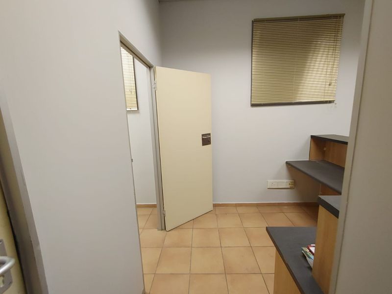 A functional office space featuring built-in desk cabinetry, tiled flooring, and window blinds, offering a clean and practical work environment.
