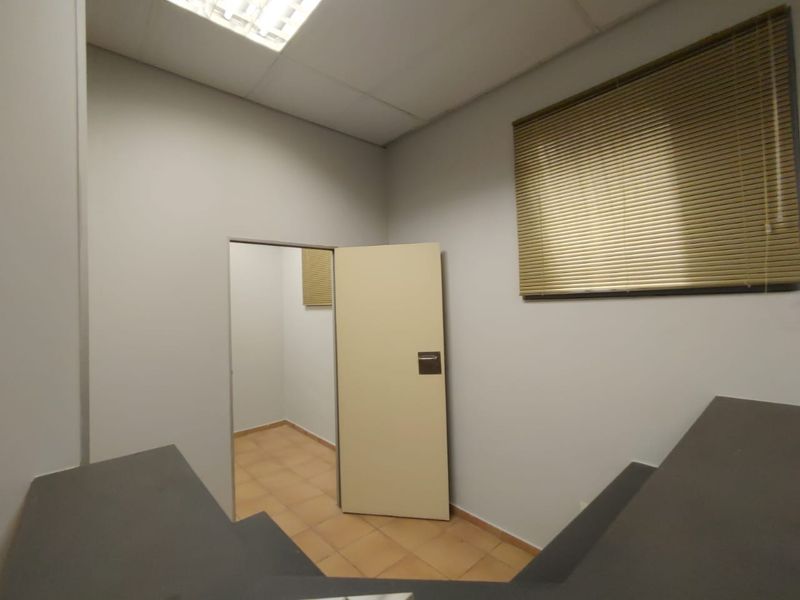 A vacant commercial office space featuring tiled flooring, a built-in counter, suspended ceiling lighting, and window blinds.