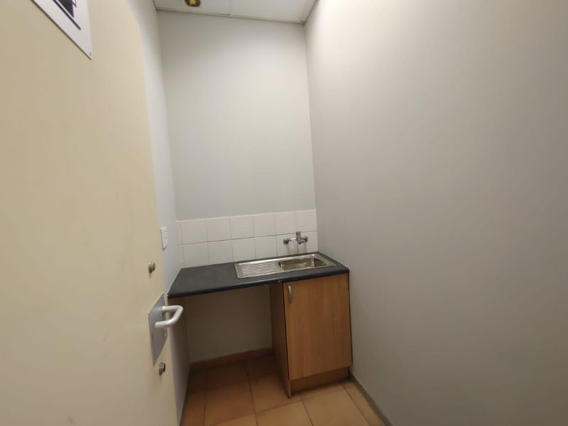A compact utility scullery area featuring a stainless steel sink, laminate countertop, base cabinetry, and tiled flooring.