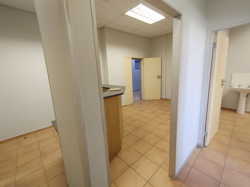 An empty commercial office space featuring tiled flooring, a built-in reception counter, and a separate washroom area with a pedestal sink.