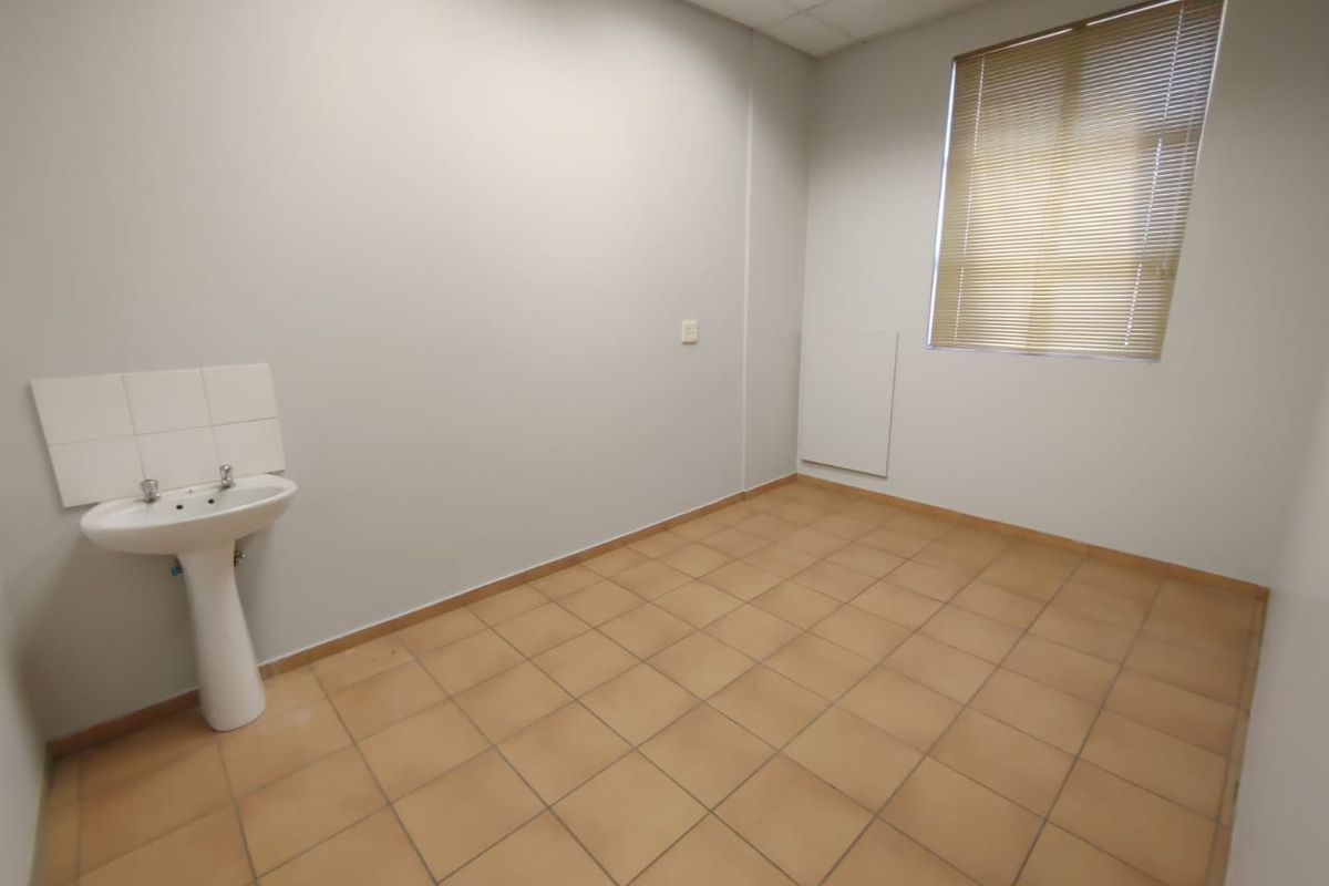 A clean, empty utility space featuring tiled flooring, a pedestal basin, and a window with fitted venetian blinds.