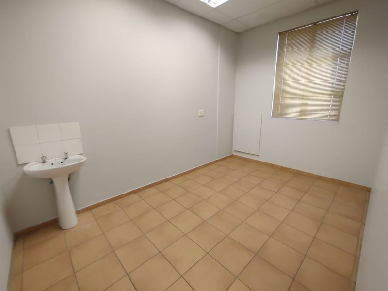 A clean, empty utility space featuring tiled flooring, a pedestal basin, and a window with fitted venetian blinds.